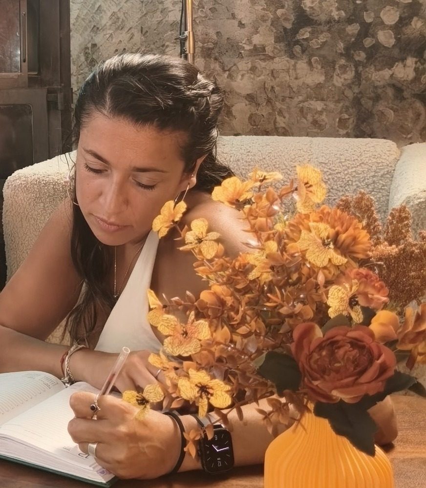 Gise escribiendo en su cuaderno junto a flores
